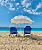 Na pierwszym planie stoją dwa leżaki na plaży, nad nimi parasol